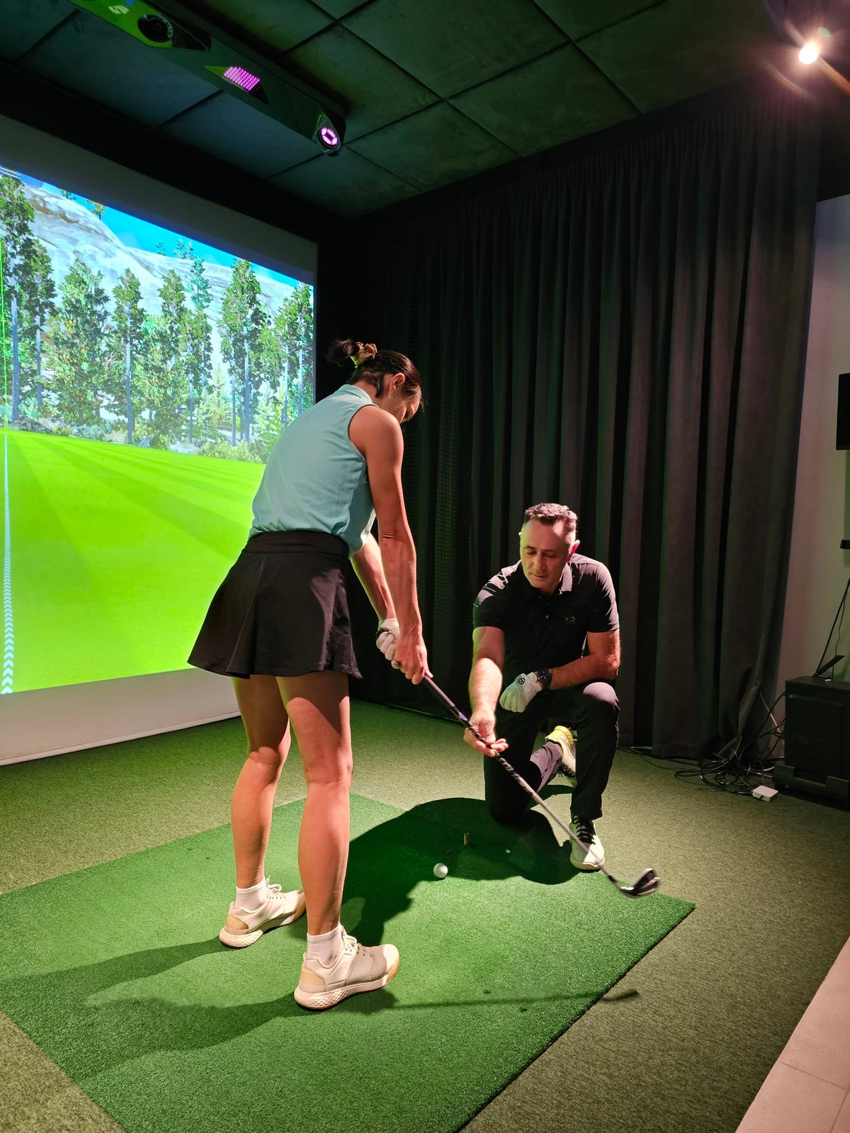 Experienced golfer teaching a beginner in a golf simulator setting with a virtual course